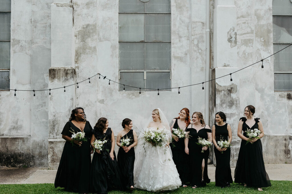 A bride with their wedding party all holding bouquets and smiling 
