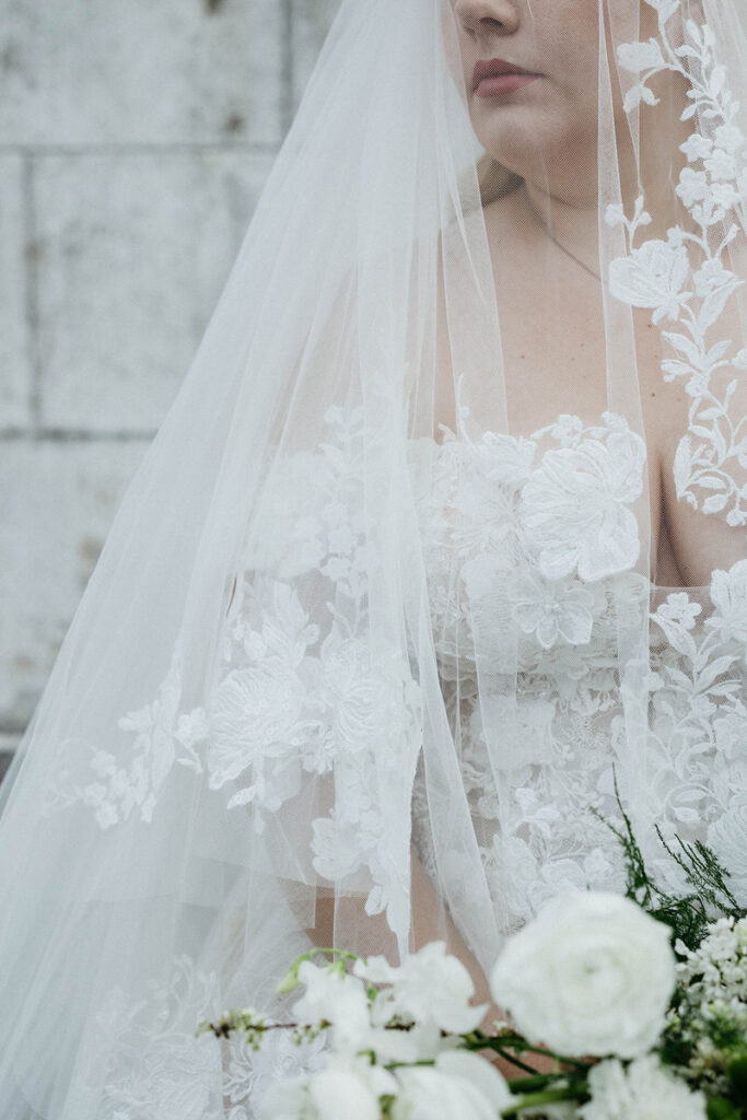 A close up of the top of a brides dress with a veil over her head 
