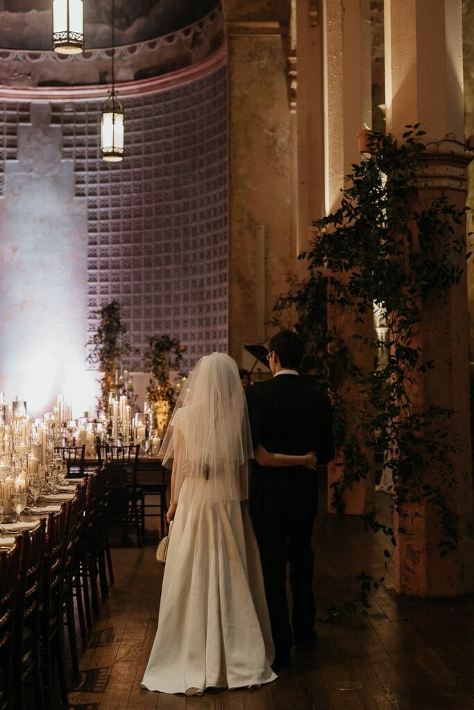 A bride and groom standing together, looking at the candlelit reception tables.
