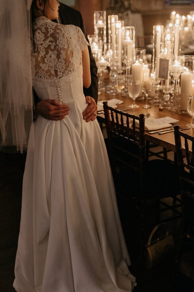 The back view of the bride and groom embracing, focusing on the intricate lace details of the bride's dress.
