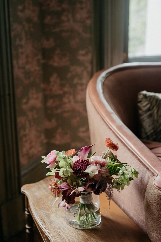 A small bouquet of mixed flowers in a glass vase, placed on a wooden table near a sofa.
