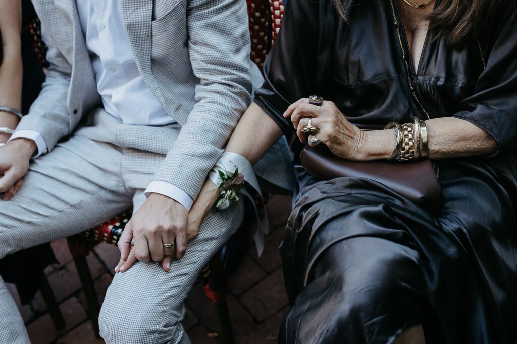 Close-up of a couple holding hands, dressed formally, with the woman's hand resting on the man's knee.
