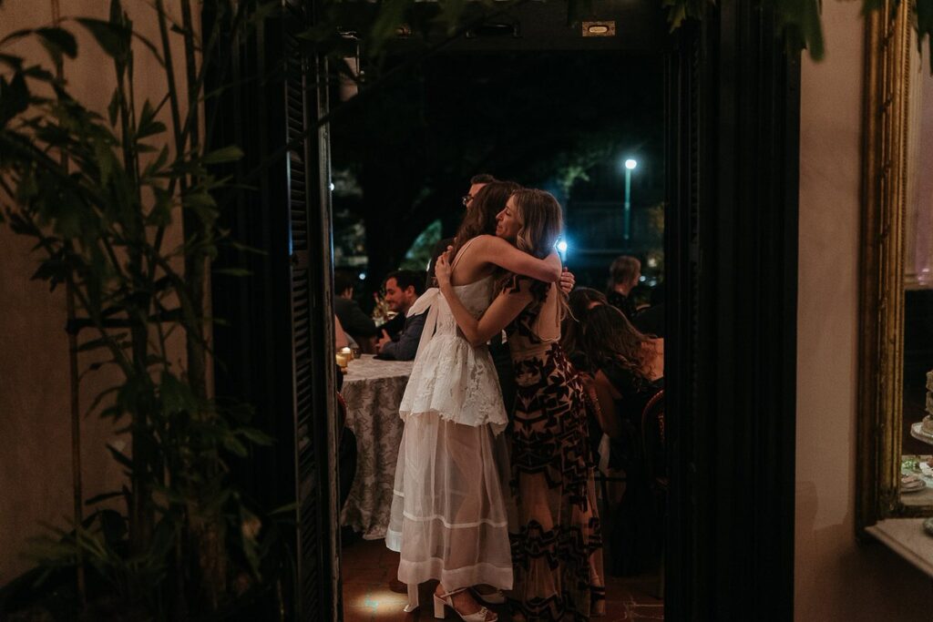 The bride hugs a guest during the evening reception, surrounded by other guests.
