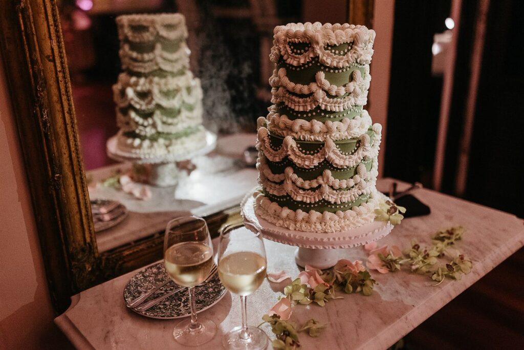 Close-up of the wedding cake with two glasses of white wine in front, reflected in a mirror behind.
