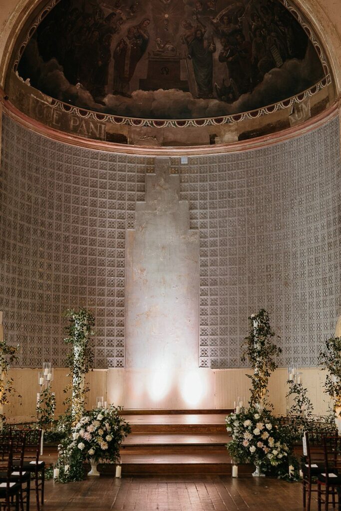 A beautifully decorated altar with floral arrangements and lighting in a historic venue.
