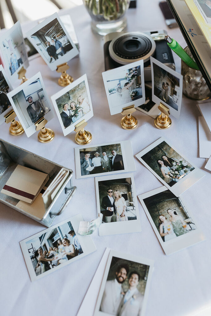 Table with Polaroid photos on display, each photo showing different moments and guests at the event. A vintage camera and some metallic trays are also part of the arrangement