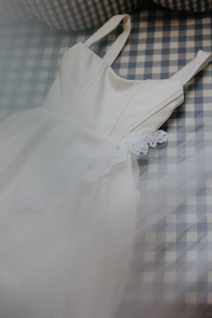 A wedding dress with lace details, laid out on a checkered bedspread.
