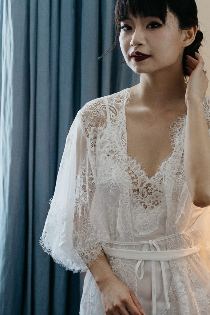 A person in a white lace dress with one hand on their neck 
