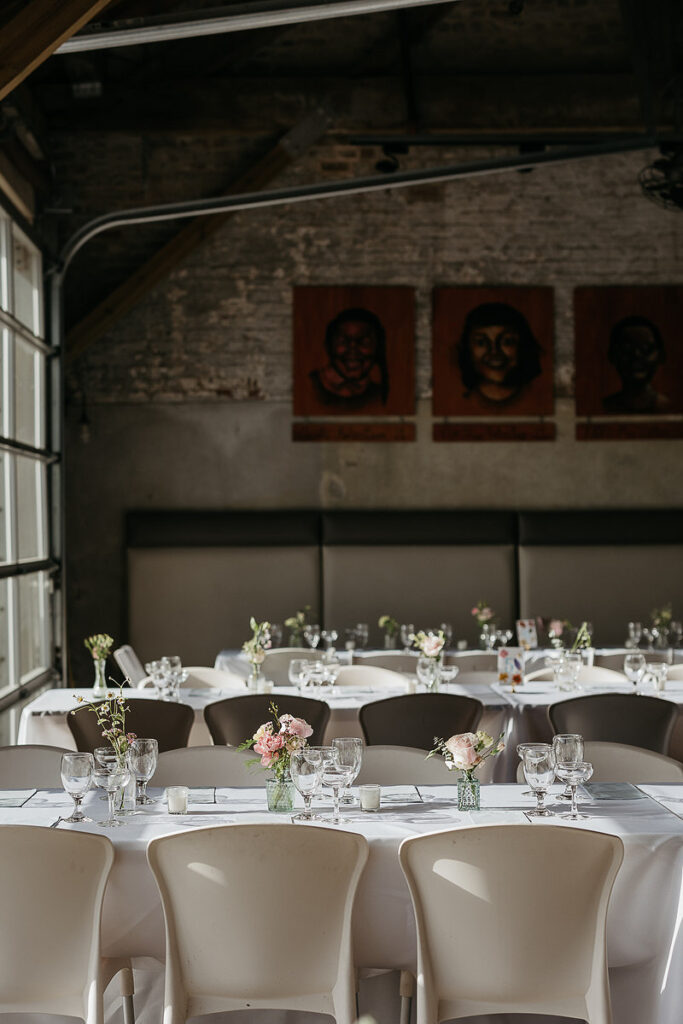 Elegantly set tables inside a venue, decorated with small floral arrangements in glass vases