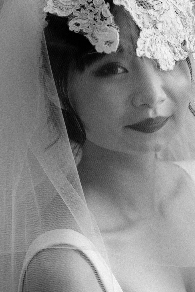 Black and white detail photo of a bride with a veil over their face 