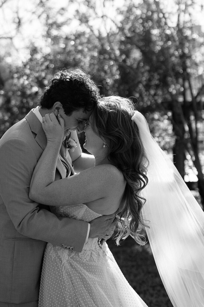 A couple sharing an intimate moment outdoors, with the bride’s veil flowing in the breeze and both smiling affectionately at each other