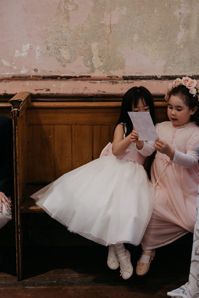 Two young girls sitting on a bench looking at a piece of paper 
