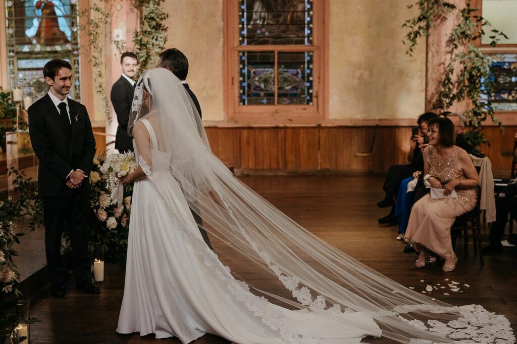 A groom smiling at a bride as she walks down the aisle 