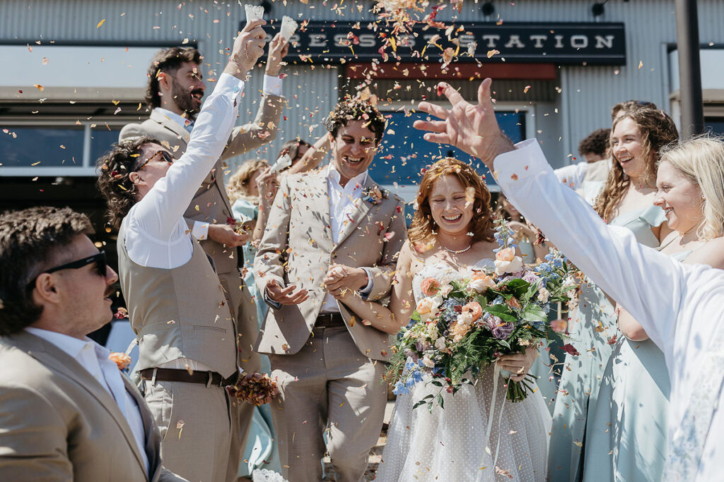 Bride and groom surrounded by friends and family, smiling as they are showered with flower petals