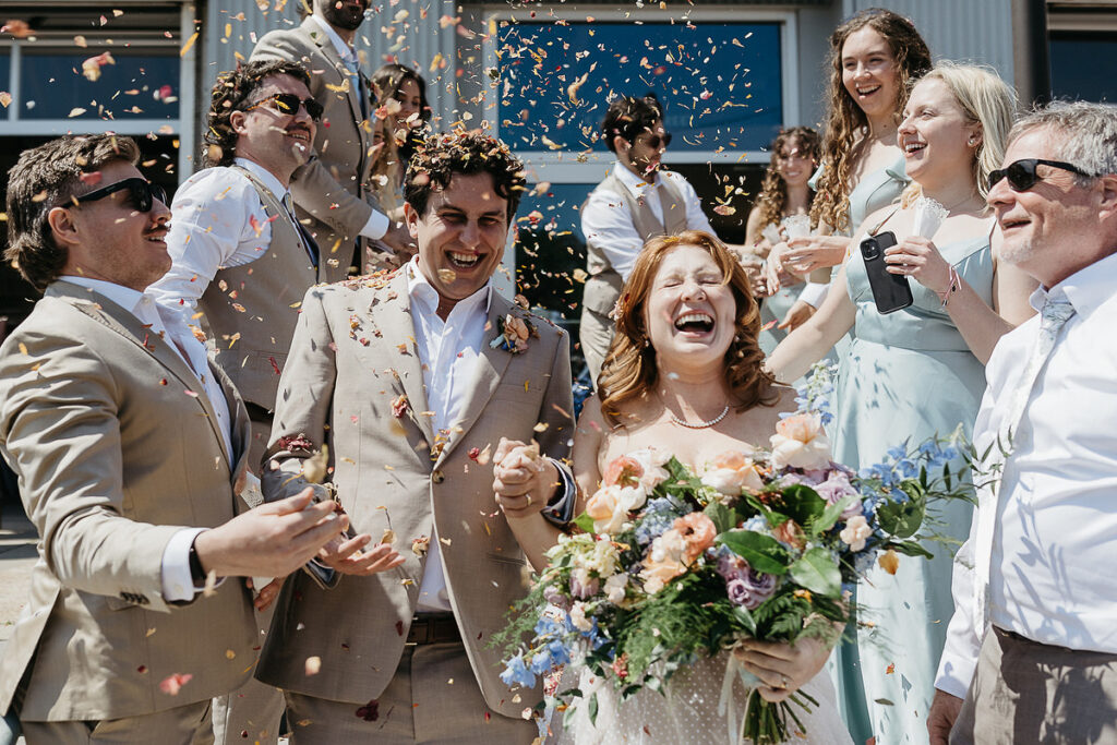 Close-up of the bride and groom laughing and celebrating with their guests while being showered with flower petals