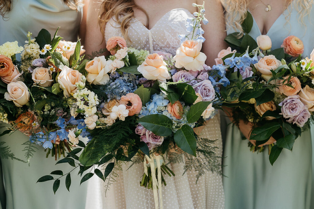 Close-up of the bride and bridesmaids holding bouquets of pastel flowers and greenery.
