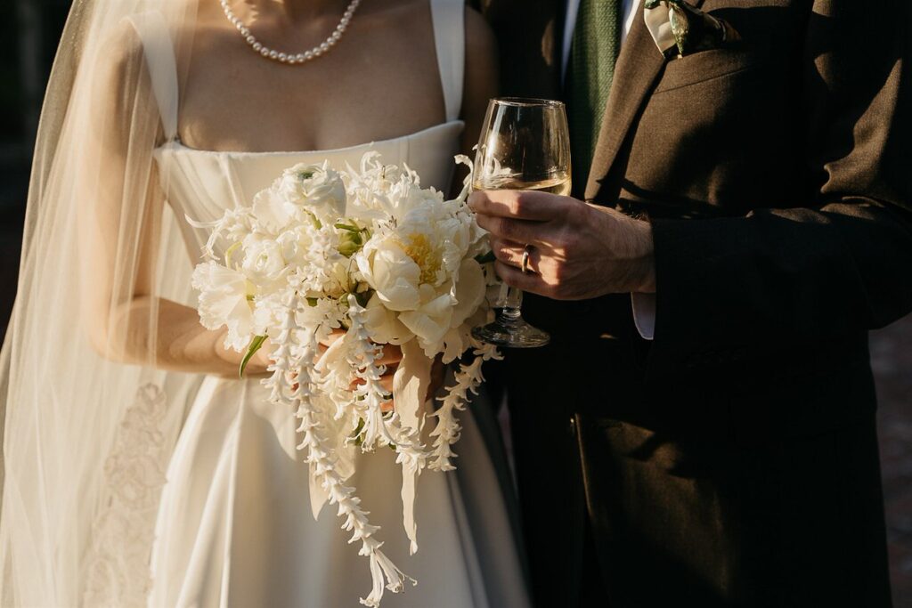 Close up of a person holding a bouquet with another person holding a wine glass next to it 