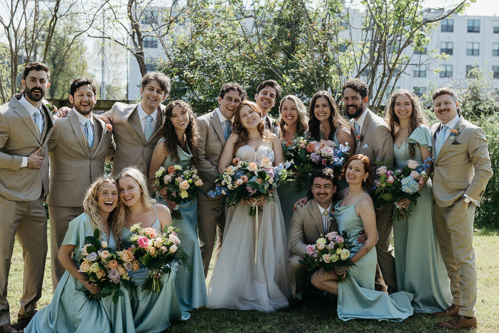 The bride and groom pose with their wedding party while everyone smiles