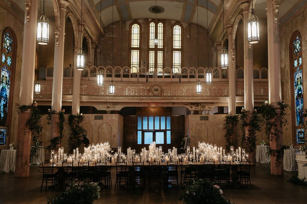 Long rectangular reception tables with candles on them set up in a grand hall 