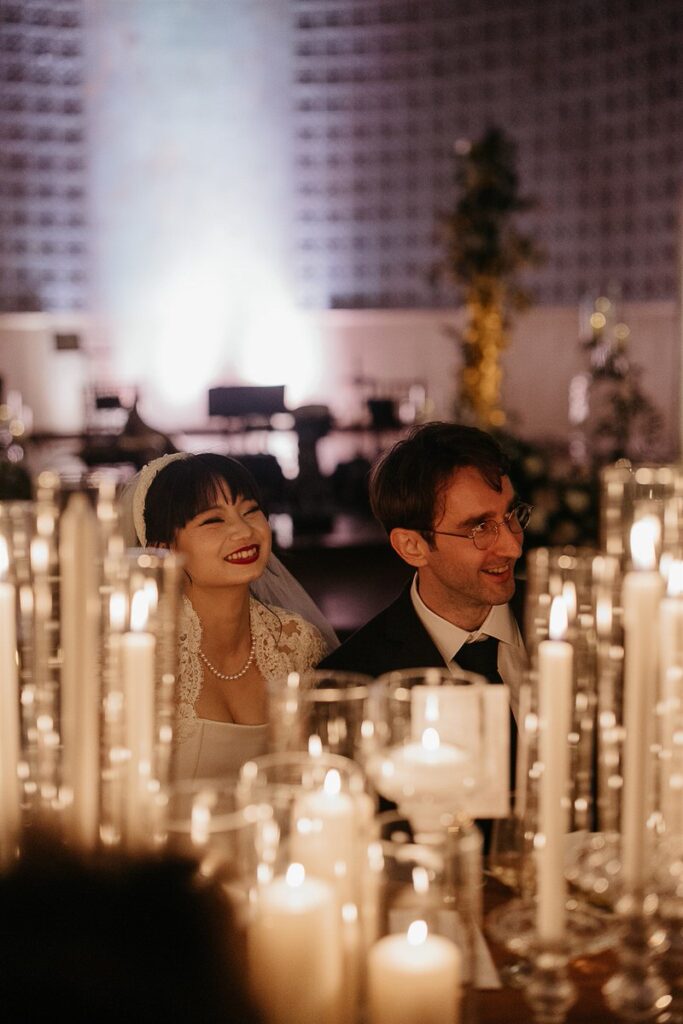 Bride and groom sitting at a reception table laughing 