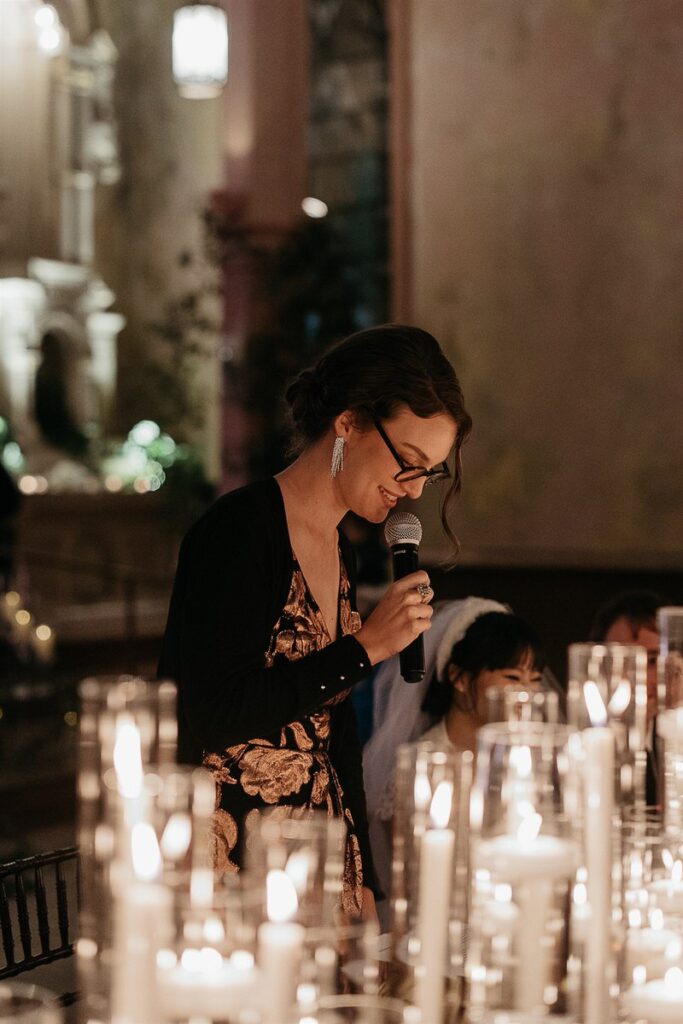 A person smiling and holding a mic as they give a speech at a wedding 