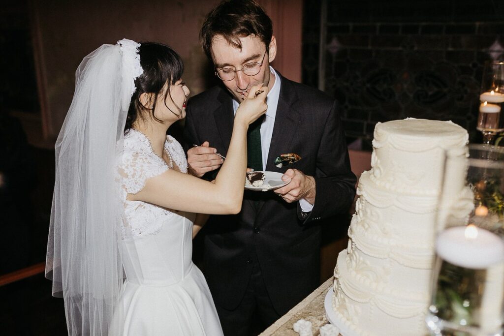 A bride feeding a groom wedding cake 