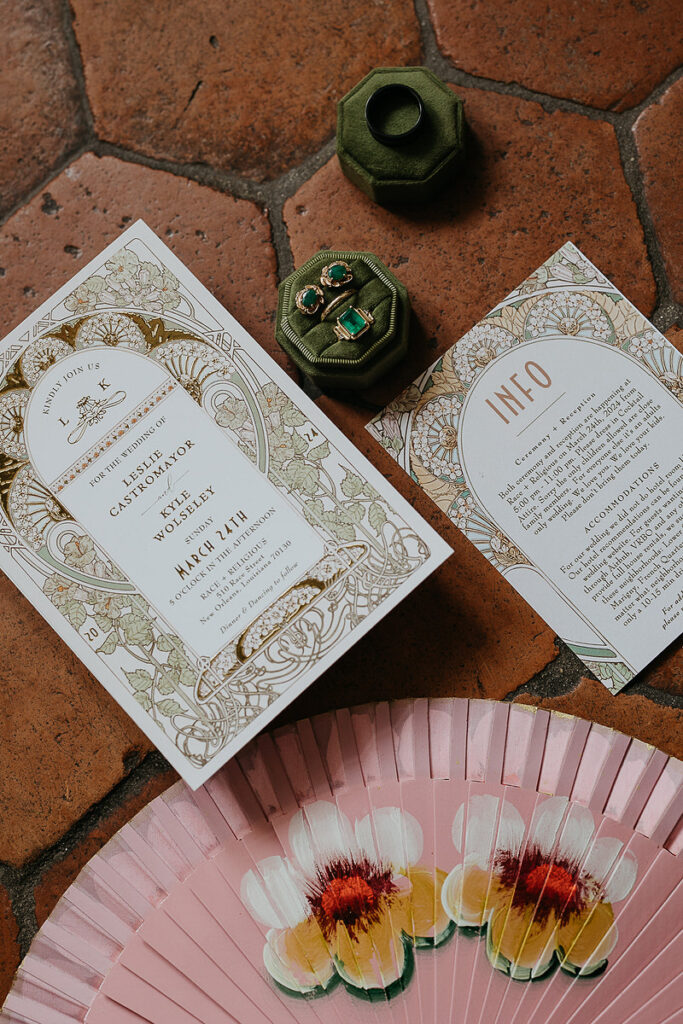 Wedding invitations and a ring box with earrings and wedding rings laid on red tile. 