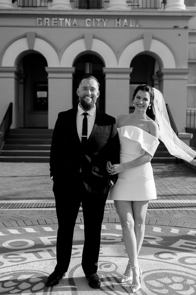 A bride with their arm looped through their partner's arm as they both smile 