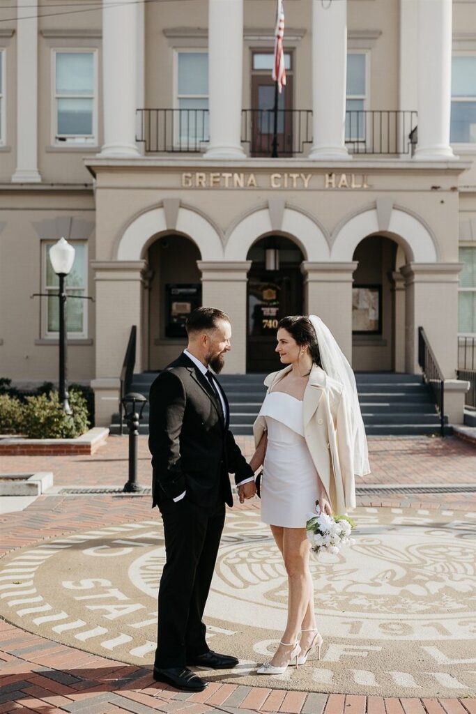 A couple holding hands and standing in front of city hall after eloping 