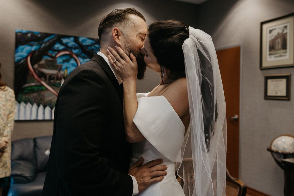 A newlywed couple during their first kiss in a courthouse 
