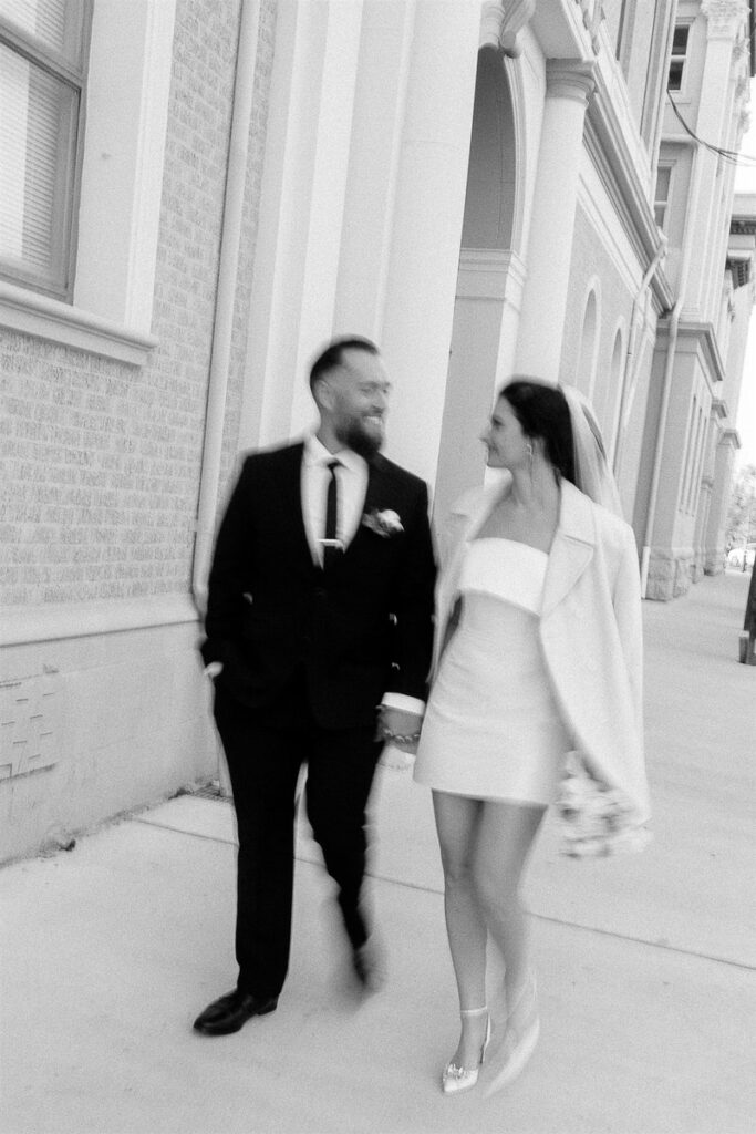 A slightly blurred photo of a newlywed couple holding hands and walking down the street 
