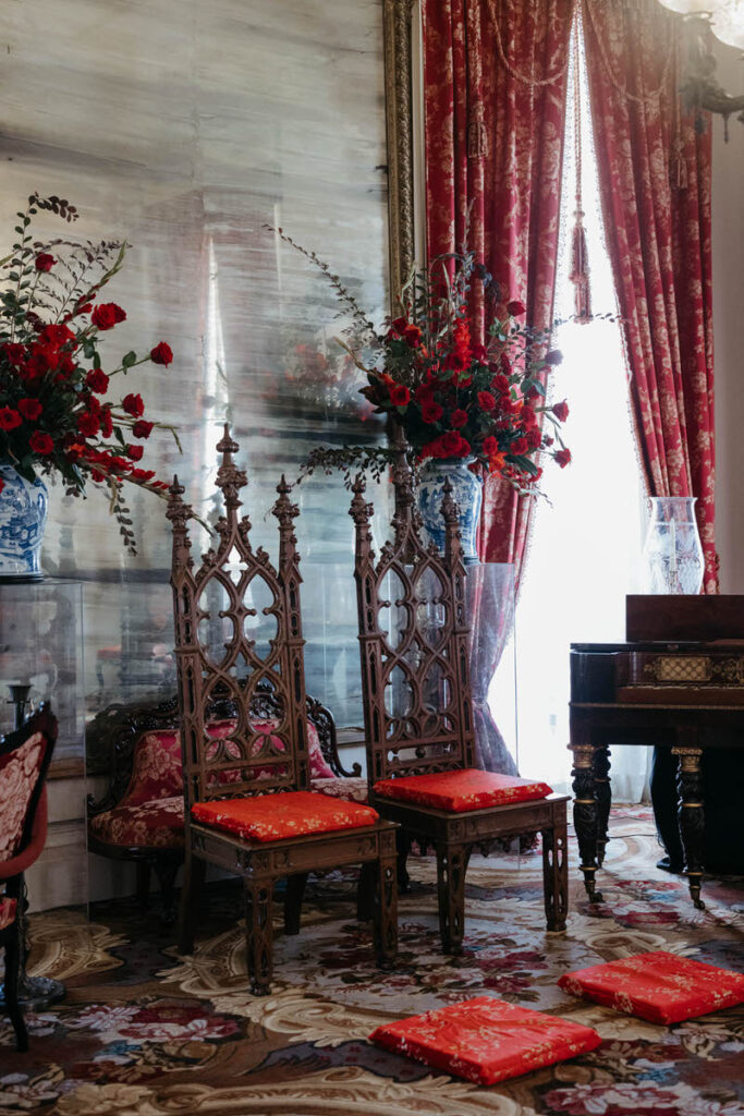 Two ornate wooden chairs with red cushions on the chairs and the floor in front of them 