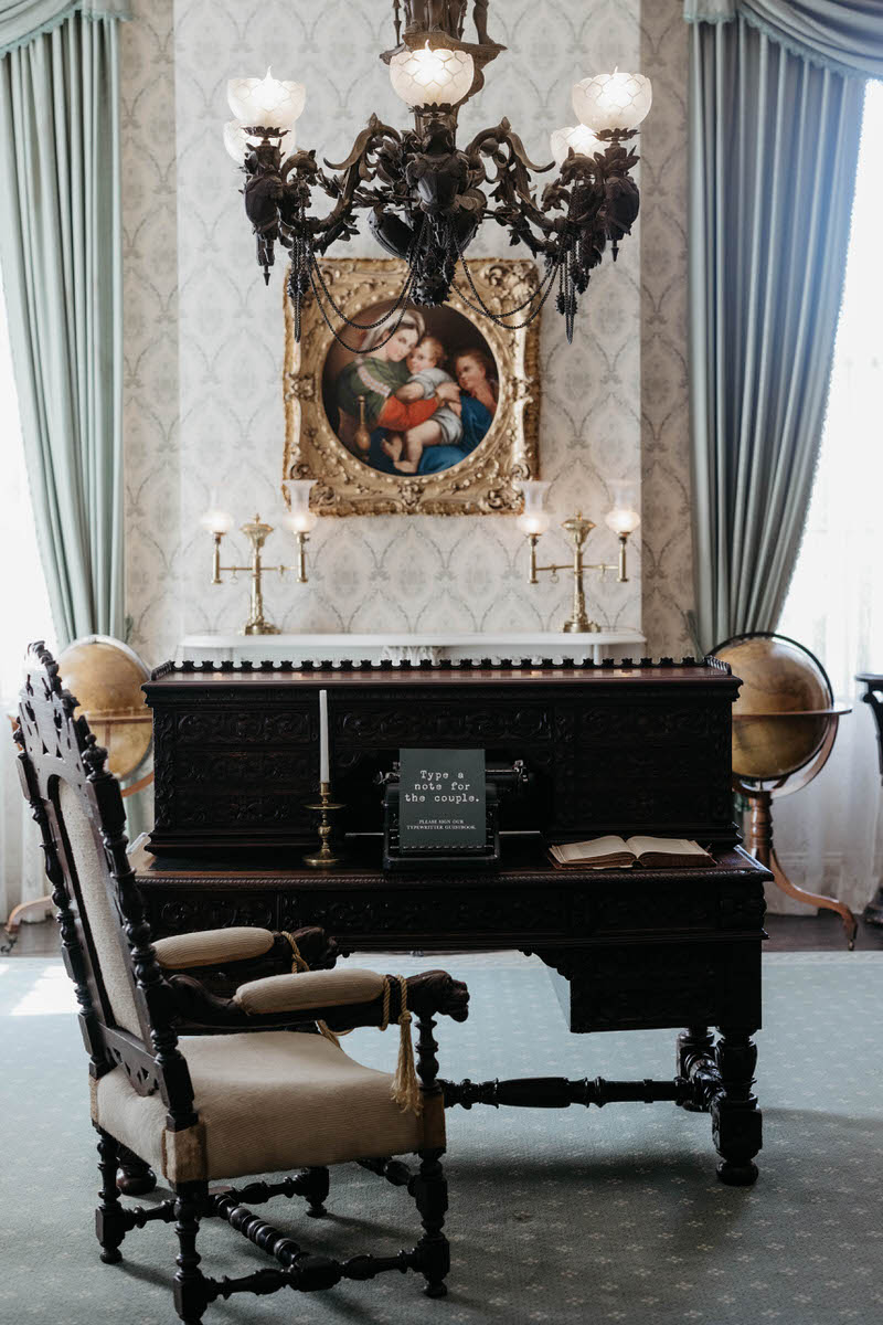 An olden wooden desk with a chair in front and a typewriter with a sign that says "Type a note for the couple."
