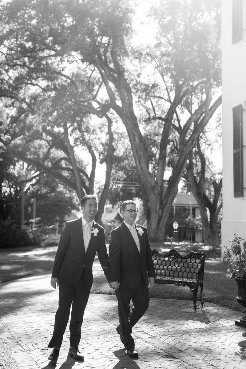 A newlywed couple holding hands and walking on a brick path 