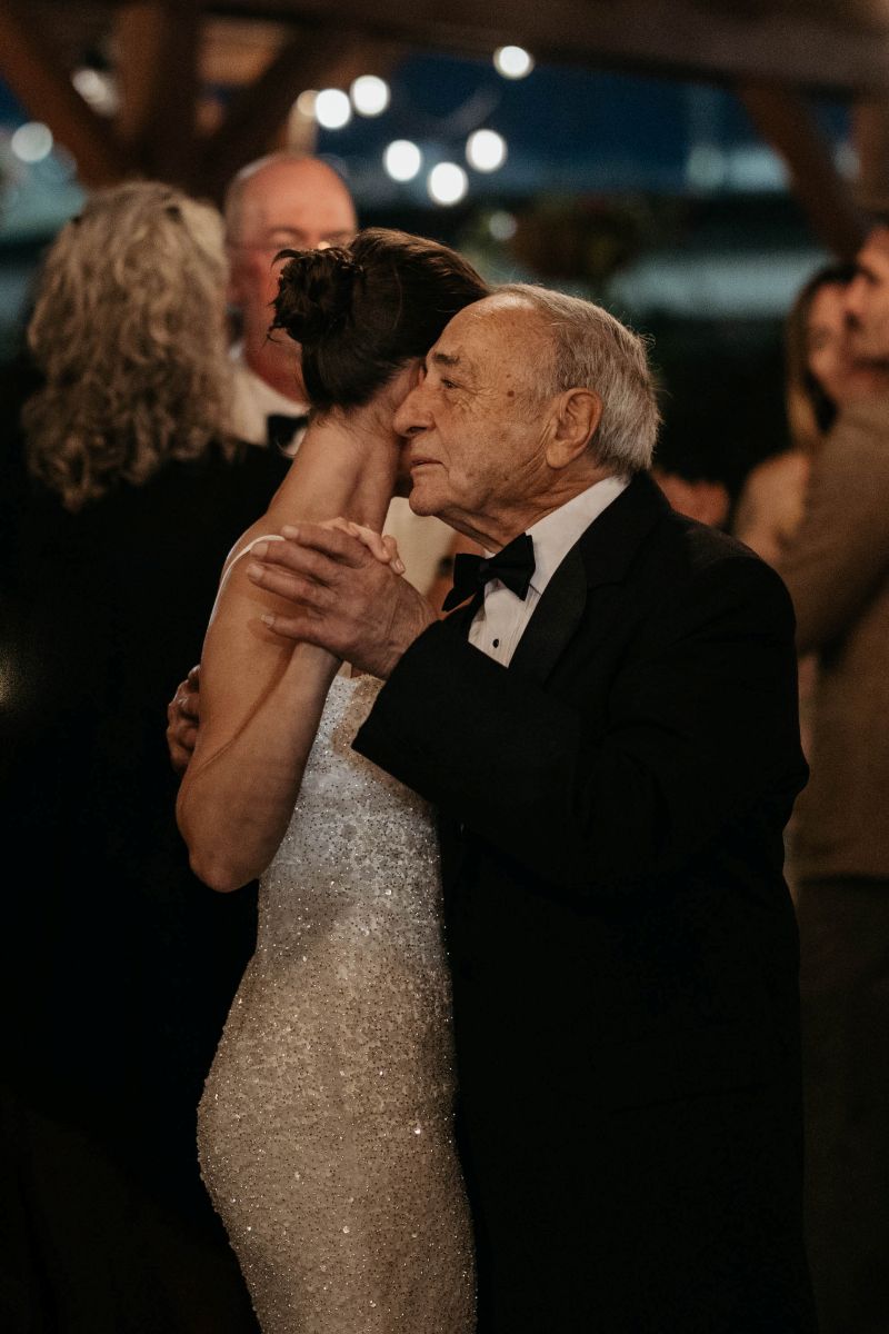 a woman in a white dress dancing with an older man at her wedding reception 