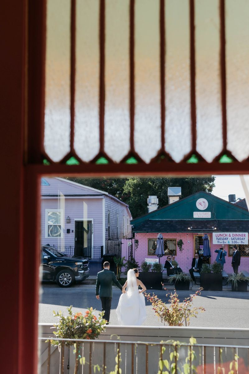 a woman in a wedding dress and white veil walking across the stree holidng hands towards a restaurant 