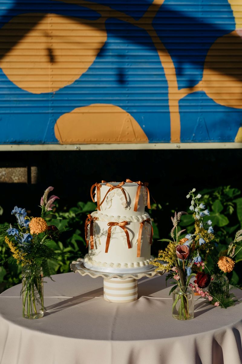 a wedding cake on a table that is covered in a tablecloth there are also flowers in vases on display 