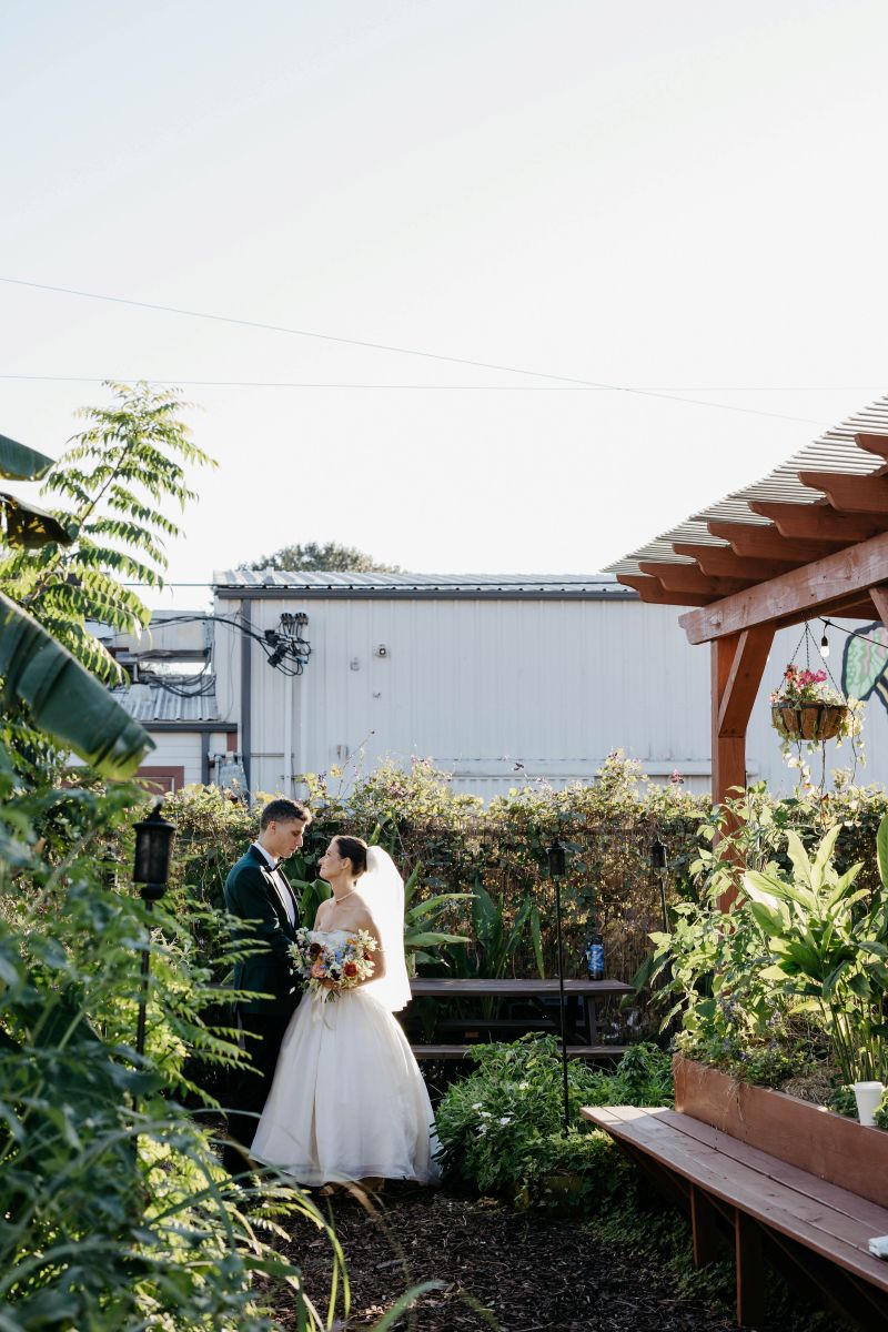 a couple standing in a garden looking into each other's eyes the woman is wearing a white wedding dress and veil and holding a bouquet of flowers the man is wearing a suit 