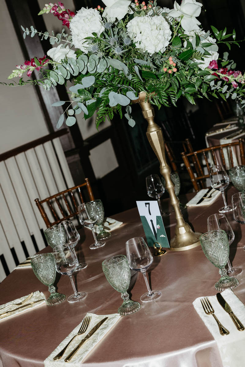 A slightly off kilter photo of a reception table with glassware and a floral arrangement on it 