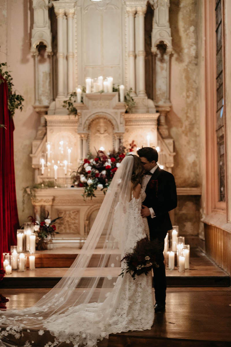 A newlywed couple kissing in front of a small altar with flowers and candles on it