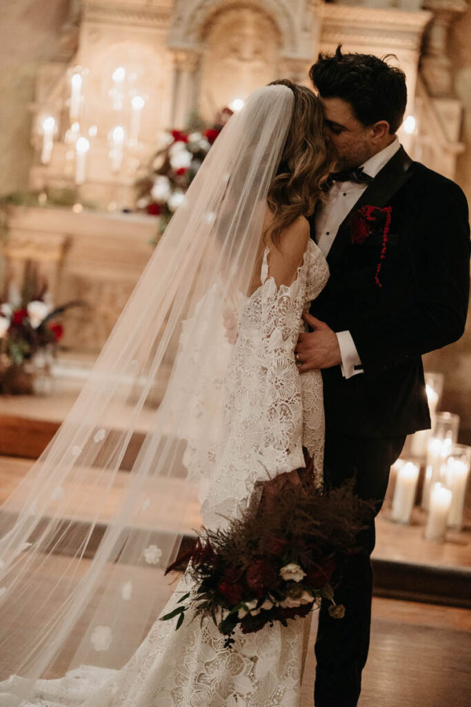 A newlywed couple kissing in front of an altar covered in florals and candles