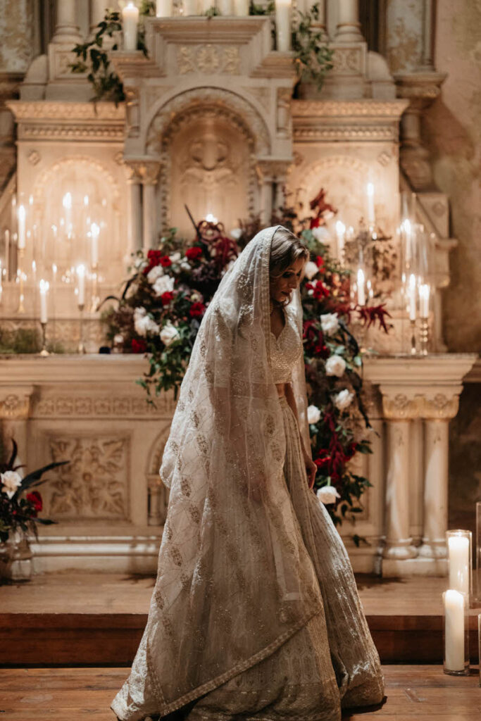 A person in a wedding dress walking in front of an altar with florals and candles on it