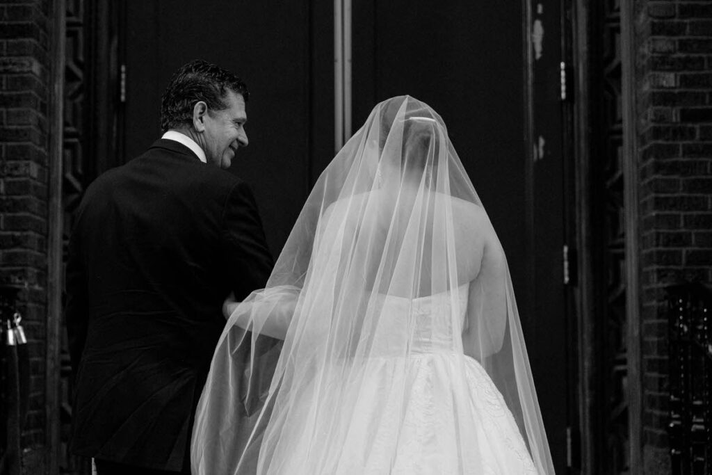 A person in a wedding dress walking into a building with an older man