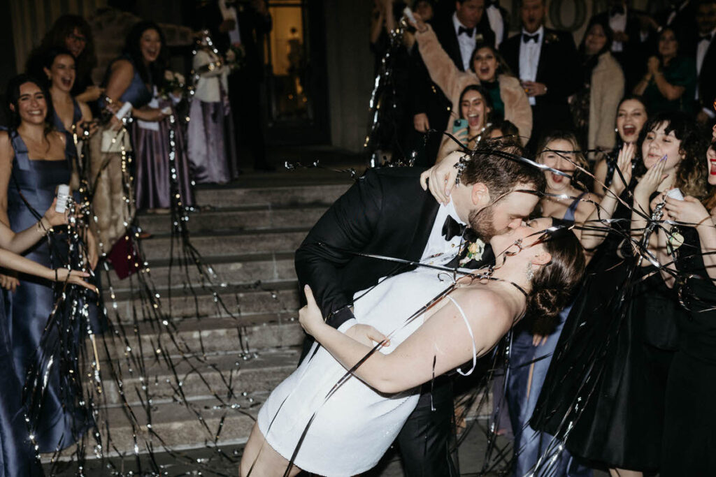 A newlywed couple kissing as guests toss streamers around them