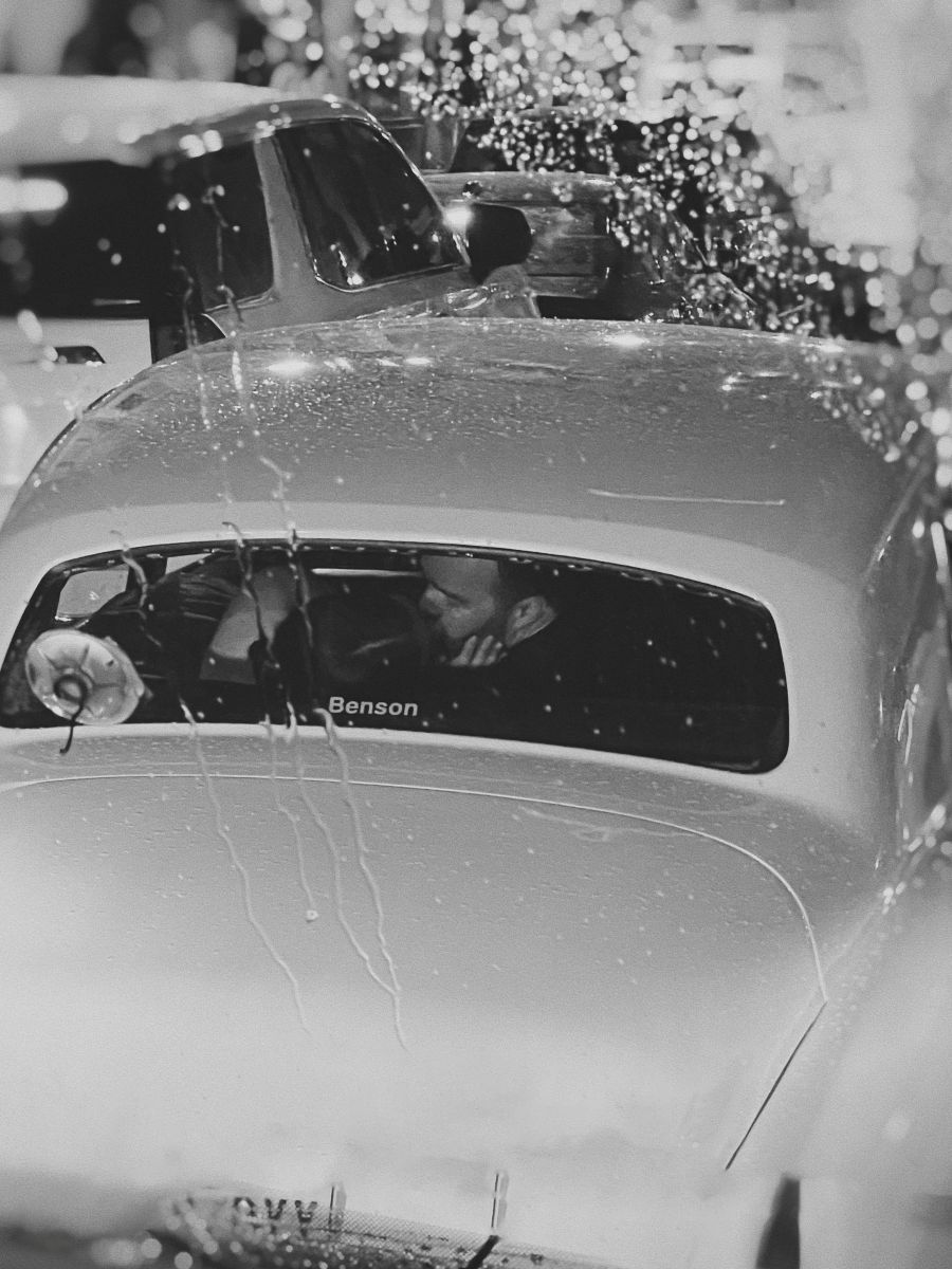 a couple kissing after their wedding ceremony in the back of car as it rains outside
