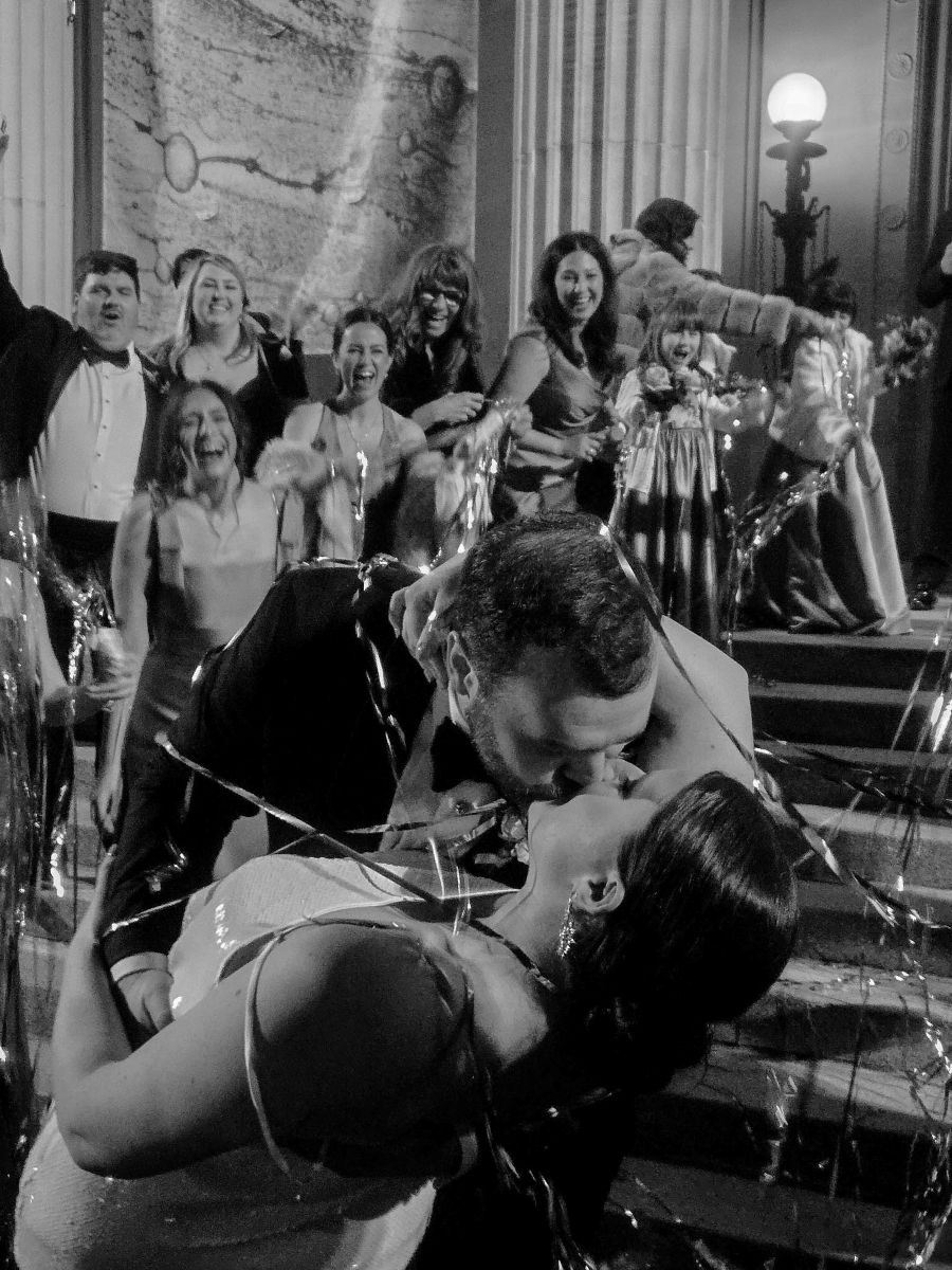 a couple kissing on steps while their wedding guests cheer for them