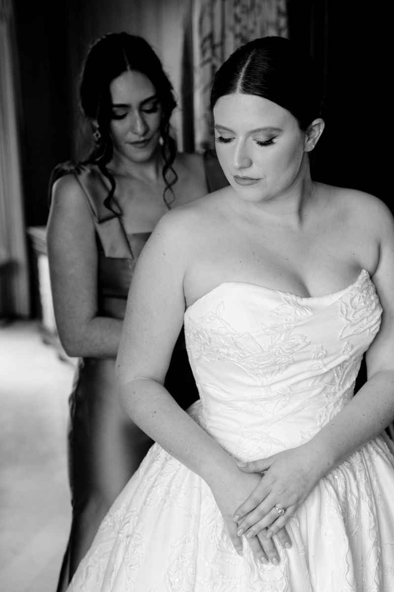 a bridesmaid helping zip a wedding dress for the bride