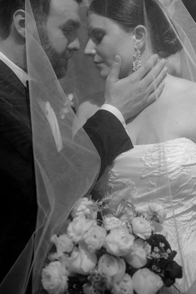 a couple taking an elegant couples potrait the man is gently touching the side of his bride's face and they are both underneath her wedding veil