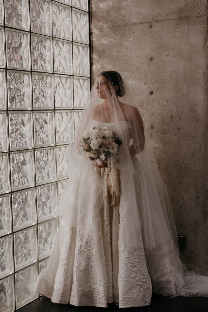 a woman posing in the cafe at the new orleans musuem of art wearing a white wedding dress and veil and holding a bouquet of flowers
