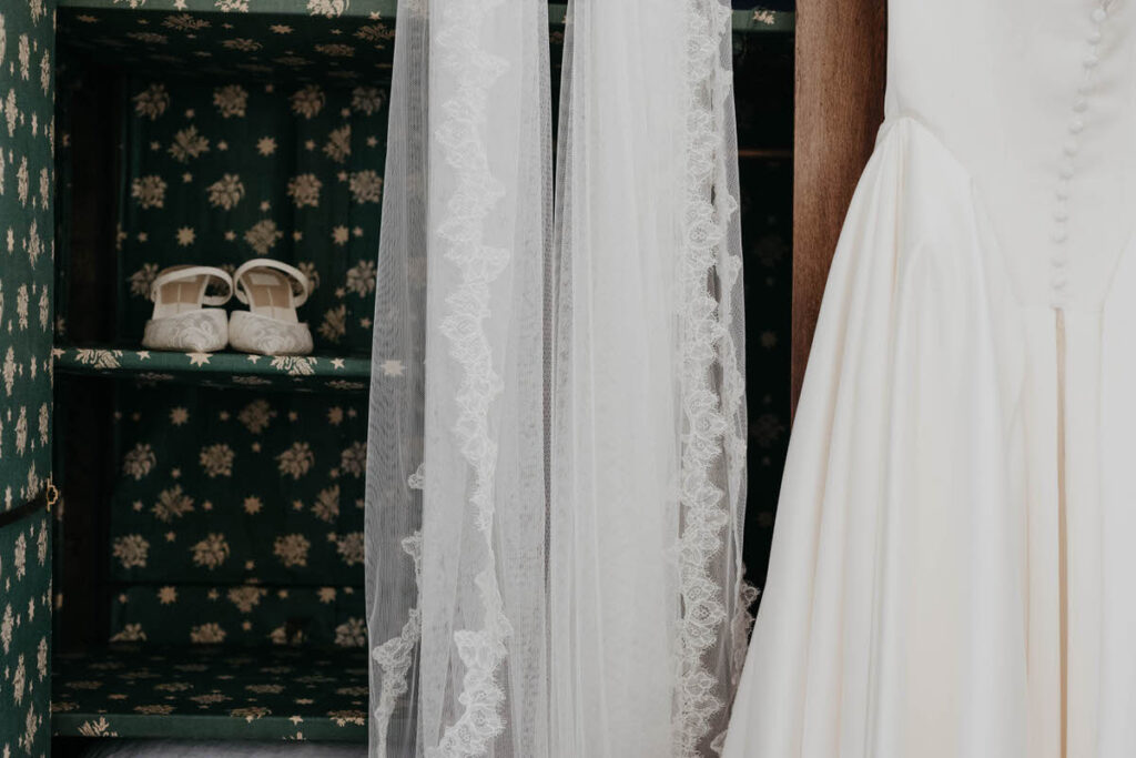 Shoes on a shelf with a veil and wedding dress hanging next to them